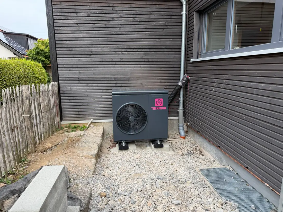 Thermion H9V1 Wärmepumpe, frisch installiert an einem Einfamilienhaus mit dunkler Holzfassade